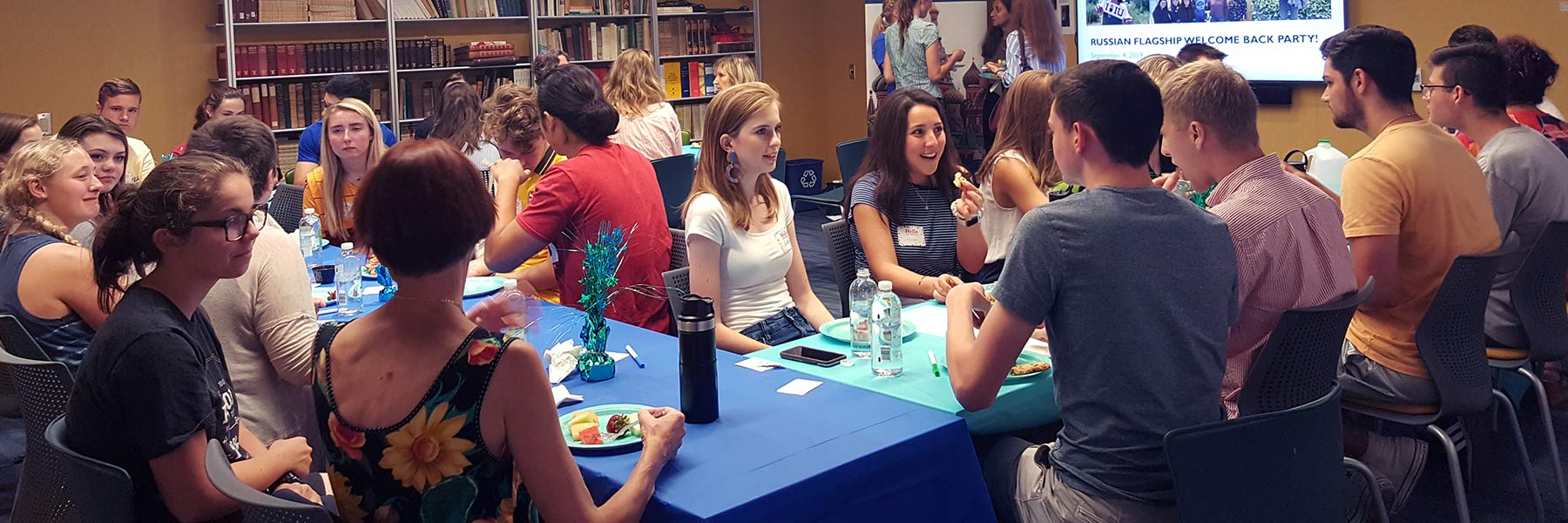 Students and staff sit around a table socializing at a Russian Flagship Program event