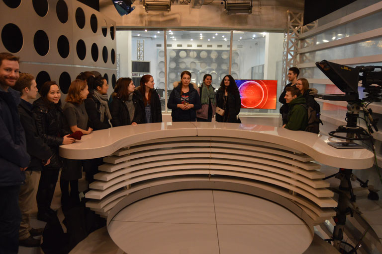 Students standing around a news desk at a television studio