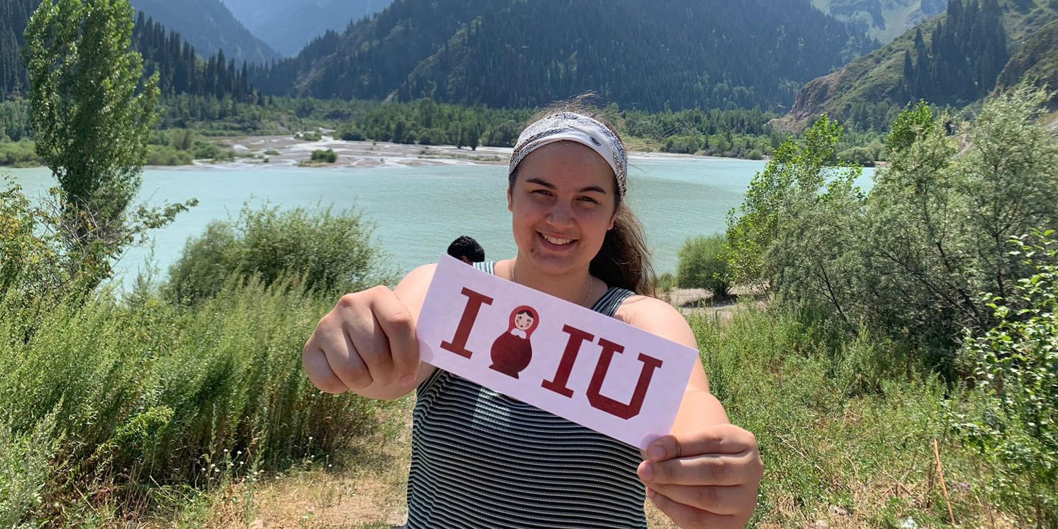 Student in the mountains holds an IU sticker