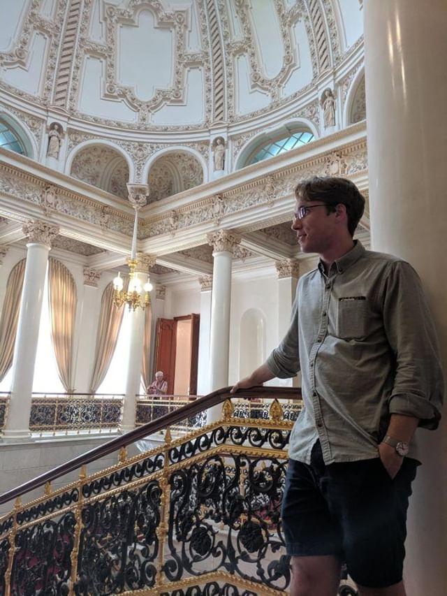 student standing at the top of a staircase in an ornate building