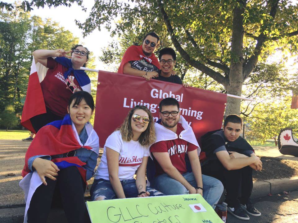 Students wearing flags as capes and holding a sign for the Global Living Learning Community