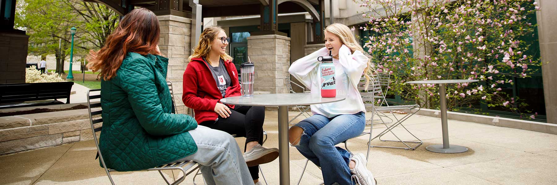 Three students sit at outdoor table conversing