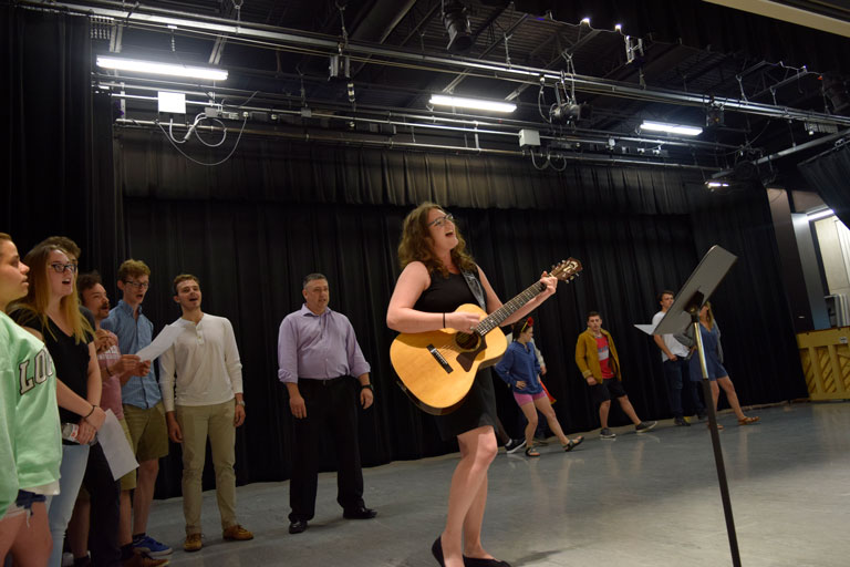 Woman playing guitar and students singing behind her